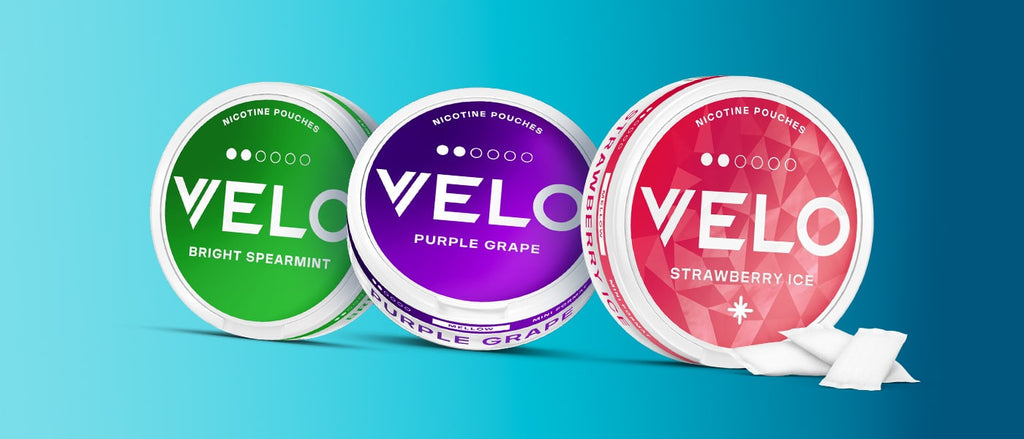 Sobre un fondo azul degradado se muestran tres sobres redondos de nicotina Velo en verde (Bright Spearmint), morado (Purple Grape) y rojo (Strawberry Ice), con sobres blancos cerca.