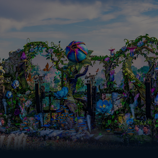 Una colorida carroza de desfile decorada con grandes flores, enredaderas, mariposas y vegetación viaja al aire libre bajo un cielo parcialmente nublado. Se ven personas cerca de la base de la carroza.
