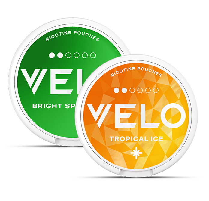 Dos envases redondos de bolsitas de nicotina VELO. El envase delantero es naranja y lleva la etiqueta Tropical Ice, mientras que el trasero es verde y lleva la etiqueta Bright Spearmint. Ambos tienen dibujos geométricos blancos.