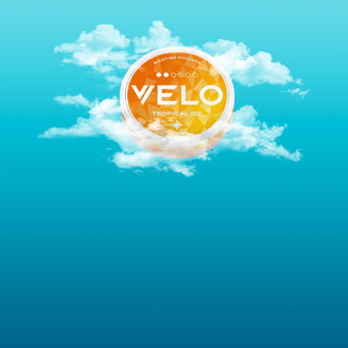 Una lata redonda de color naranja con la etiqueta "VELO Tropical Ice" rodeada de esponjosas nubes blancas flota sobre un fondo de cielo azul brillante.