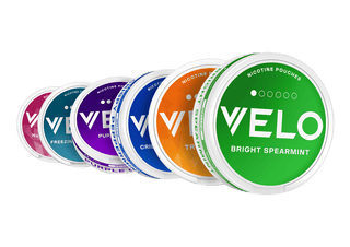 Seis latas redondas de bolsitas de nicotina VELO están dispuestas en línea diagonal, cada una de un color diferente: verde, naranja, azul, morado, verde azulado y rosa, con nombres de sabores visibles como Bright Spearmint y otros.