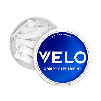 Un envase VELO Crispy Peppermint blanco redondo abierto con tapa azul revela varias bolsitas blancas. La etiqueta destaca la nicotina mentolada y los ingredientes de alta calidad para una experiencia refrescante.