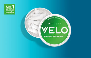 Contenedor redondo de bolsas de nicotina VELO Bright Spearmint, con la tapa parcialmente abierta para dejar ver las bolsas blancas del interior. Una etiqueta verde en la tapa y un recuadro verde a la izquierda rezan No.1 bolsas de nicotina en España.