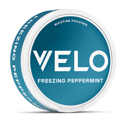 Un envase redondo, verde azulado y blanco de VELO lleva la etiqueta Freezing Peppermint y muestra "Nicotina Mentolada" encima del logotipo. El lateral destaca "Freezing Peppermint", "menta intensa" e "ingredientes de alta calidad".