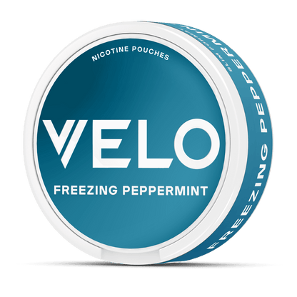 Un envase redondo azul y blanco de VELO con la etiqueta "Freezing Peppermint" presenta un texto blanco en negrita en la tapa y "Nicotina Mentolada" en la parte superior, destacando sus ingredientes de alta calidad.