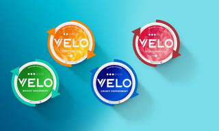 Cuatro envases redondos de nicotina VELO de distintos colores (amarillo, rojo, verde y azul) etiquetados como Tropical Ice, Strawberry Ice, Bright Spearmint y Crispy Peppermint, dispuestos sobre un fondo azul degradado.