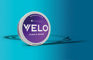 Un envase redondo con la etiqueta VELO Purple Grape Nicotine Pouches con un diseño en morado y blanco se sitúa sobre un fondo azul degradado con motivos circulares.