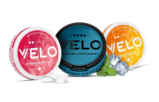 Tres envases redondos de bolsitas de nicotina VELO en sabores fresa ice (rosa), menta helada (azul) y tropical ice (amarillo), con bolsitas, hojas de menta y cubitos de hielo dispuestos delante.