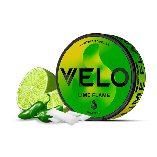 Se muestra una lata redonda de sobres de nicotina VELO Lime Flame con un diseño verde y amarillo, rodeada de sobres blancos, chiles verdes y una lima en rodajas para resaltar los ingredientes de alta calidad sobre un fondo blanco liso.