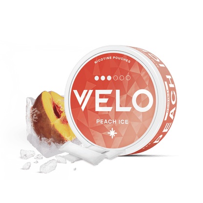 Un envase redondo de VELO Peach Ice se sitúa junto a una rodaja de melocotón y cubitos de hielo, sugiriendo jugosos melocotones. La lata naranja con texto blanco ofrece una refrescante experiencia nicotínica. Todo ello sobre un fondo blanco.