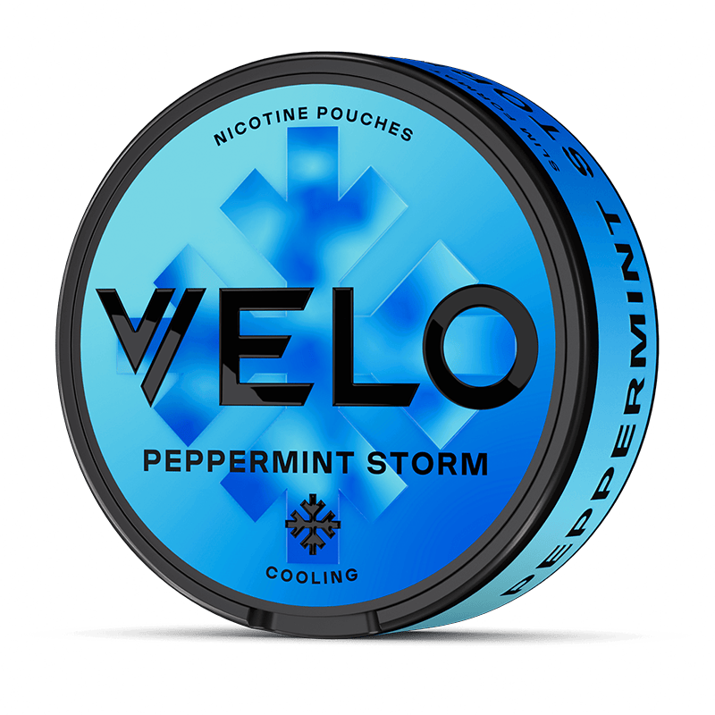 Un envase redondo azul VELO Peppermint Storm con bolsitas de Nicotina mentolada presenta un texto negro en negrita, un diseño de menta, "Cooling", y ofrece intenso sabor a menta en la tapa y en el lateral.