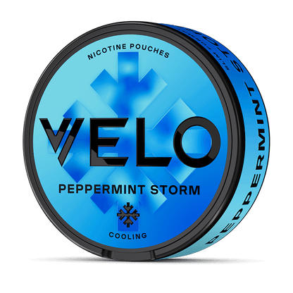 Un envase redondo azul VELO Peppermint Storm con bolsitas de Nicotina mentolada presenta un texto negro en negrita, un diseño de menta, "Cooling", y ofrece intenso sabor a menta en la tapa y en el lateral.