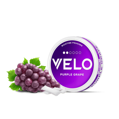 Un envase de VELO Purple Grape se muestra con uva dulce fresca y dos bolsitas blancas, destacando el envase morado y blanco del producto que sugiere un irresistible sabor afrutado a nicotina.