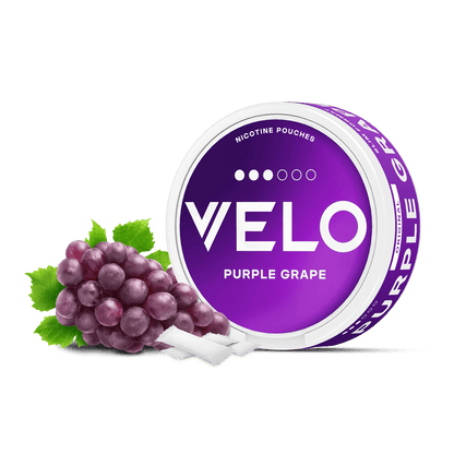 Un envase redondo VELO Purple Grape y dos bolsitas de nicotina blancas están colocados junto a un racimo de uvas moradas, todo ello sobre un fondo blanco.