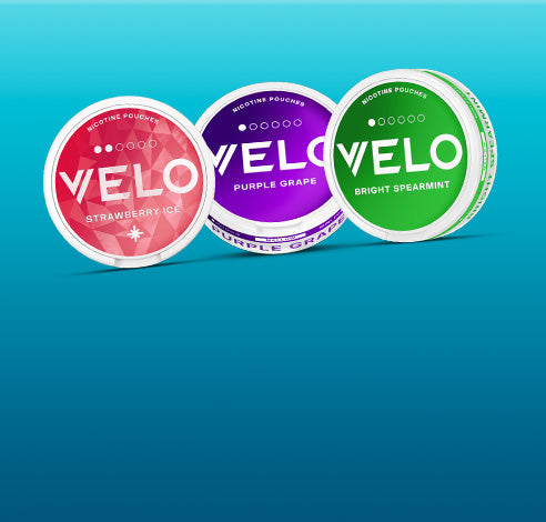 Tres botes circulares de bolsas de nicotina VELO de sabores Fresa Helada (rojo), Uva Morada (morado) y Menta Verde Brillante (verde) dispuestos sobre un fondo azul degradado.