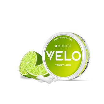 Una lata redonda, verde y blanca de VELO Tangy Lime junto a rodajas de lima y bolsitas blancas de snus sobre un fondo blanco liso.