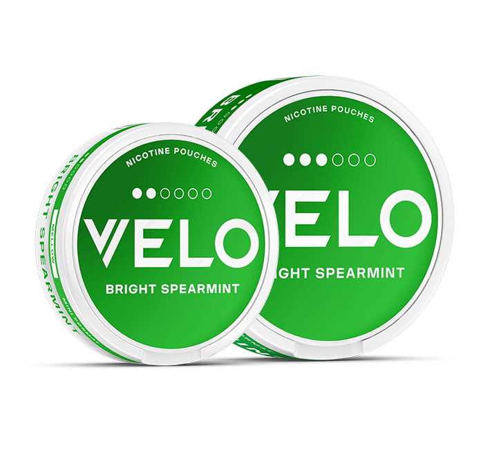 Sobre fondo blanco se muestran dos latas redondas de color verde etiquetadas como VELO Bright Spearmint y Nicotine Pouches. Las latas tienen un texto blanco en negrita y un diseño minimalista.