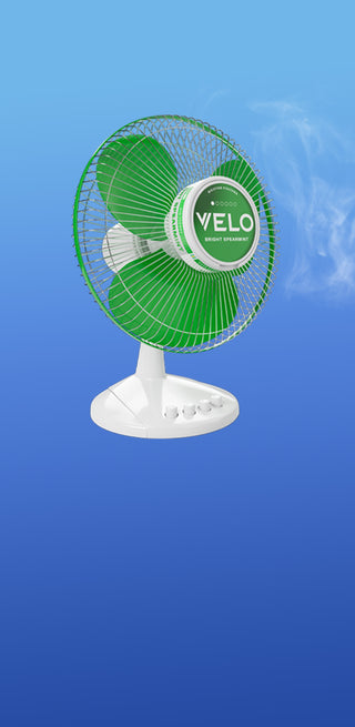 Un ventilador de mesa verde y blanco con la etiqueta VELO sopla aire, visible en forma de niebla, sobre un fondo azul degradado.