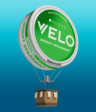 Un globo aerostático con una cesta, donde el globo es una gran lata verde de bolsa de nicotina VELO Bright Spearmint, flotando sobre un fondo azul degradado.