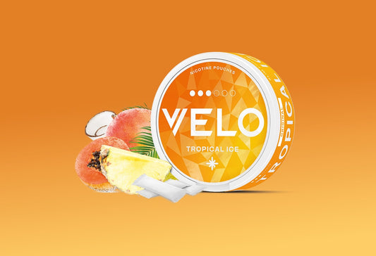 Un envase redondo con la etiqueta VELO Tropical Ice sobre fondo naranja, rodeado de imágenes de un coco, un melocotón, una rodaja de piña y una hoja de palmera, con dos bolsas blancas delante.