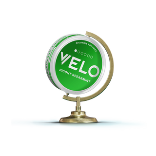 Una bolsa de nicotina verde VELO Bright Spearmint se muestra en posición vertical sobre un soporte dorado que se asemeja a un pequeño globo terráqueo, sobre un fondo blanco.