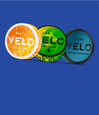 Sobre un fondo azul se muestran tres envases de bolsa de nicotina VELO: Tropical Ice (naranja), Lime Flame (verde) y Freezing Peppermint (azul).
